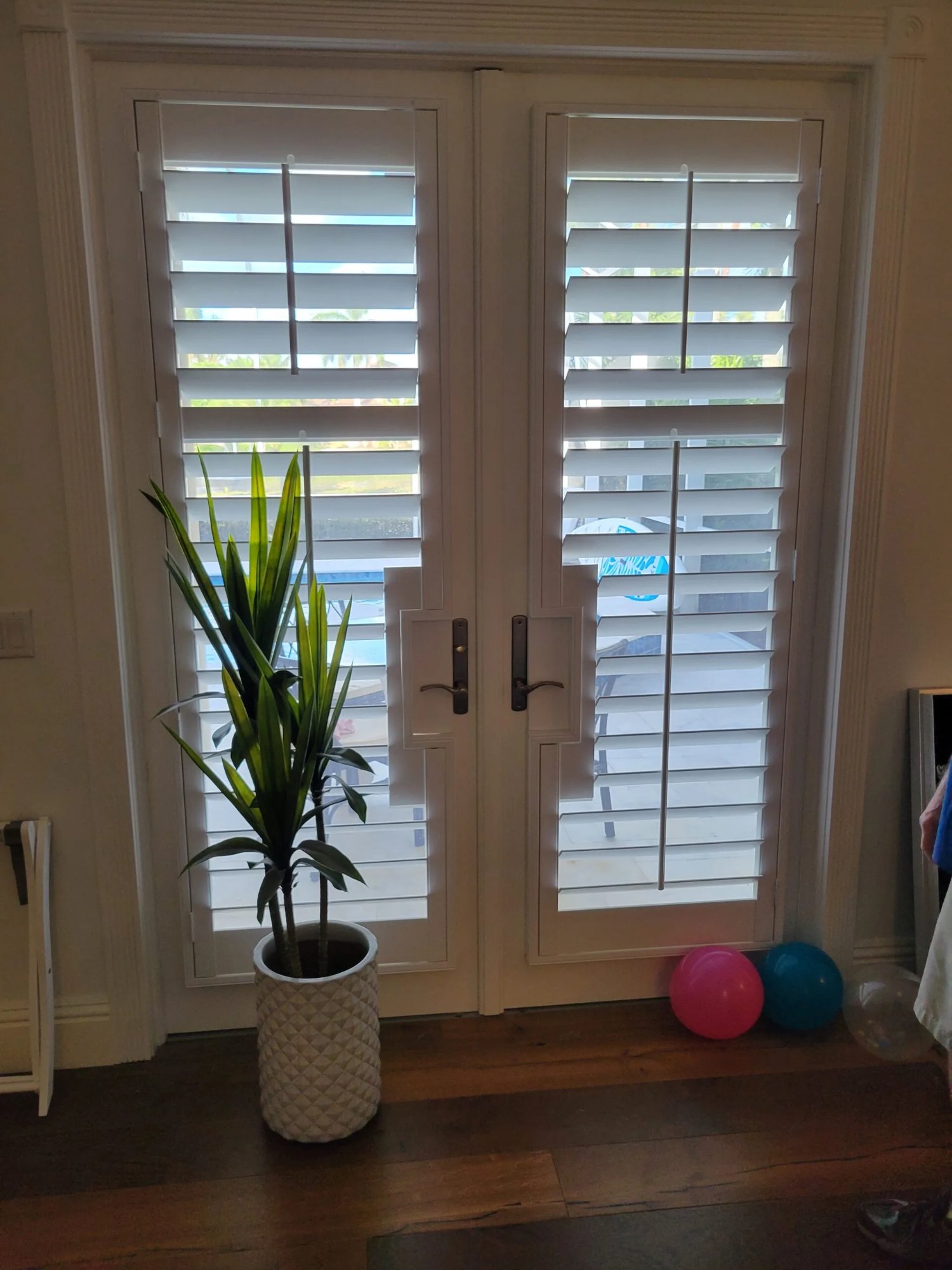 White plantation shutters on French doors with pool view in a South Florida home